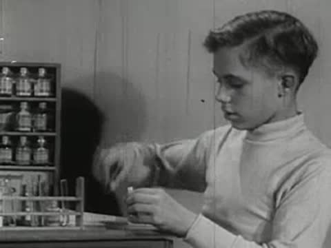 Boy performing chemistry set experiments at dresser in bedroom.