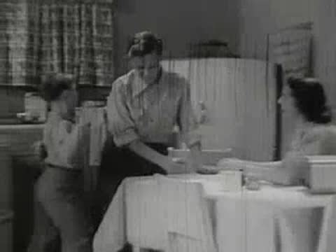 Woman tending to boy at kitchen table while another boy watches