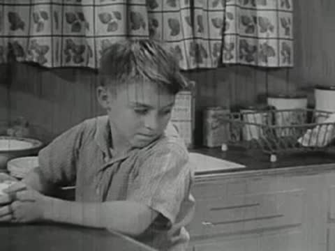 Boy leaning on kitchen counter looking unhappy, interior
