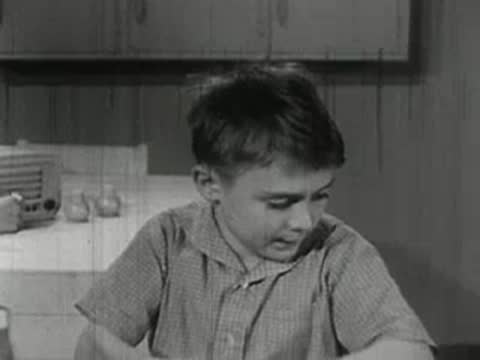 A child washing dishes at a kitchen sink with another child watching.