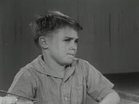 A young boy sitting and looking pensive, slightly frowning.