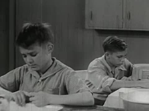 A young boy sitting at a table, thinking and holding his hands together.