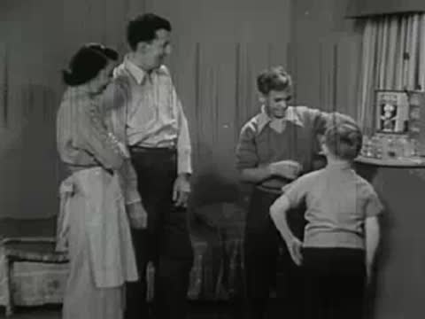 A family watching an older boy work with chemistry equipment at a counter.