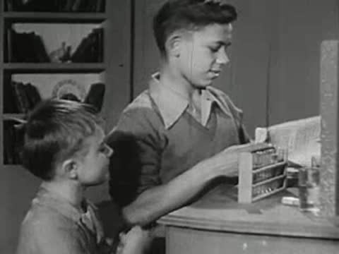 An older boy showing a chemistry notebook to a younger boy.
