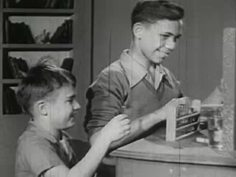 An older boy sharing chemistry equipment with a younger boy at a counter.