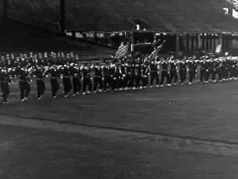 Marching band parade on a field, military precision formation, 1950s documentary.