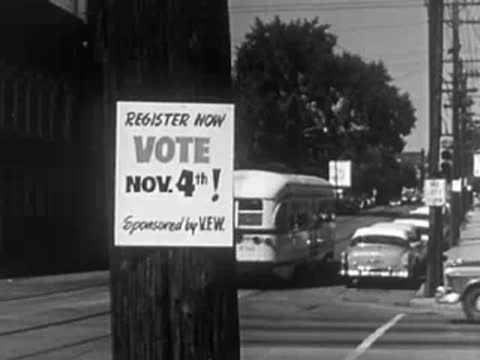 Person walking away after pasting voting poster on utility pole, street traffic.