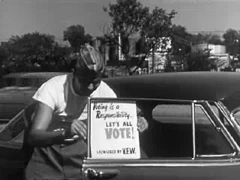 Person putting election campaign sign in car window, 1950s street.