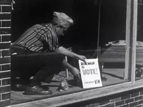 Person placing "Remember to Vote!" sign in storefront window, 1950s.