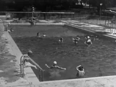 Children playing and swimming in an outdoor public pool, 1950s.