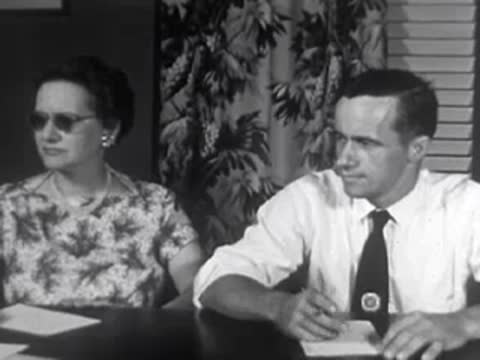 Man and woman sitting at meeting table, writing and listening, 1950s.