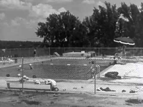 Outdoor public swimming pool with people relaxing and swimming, 1950s.