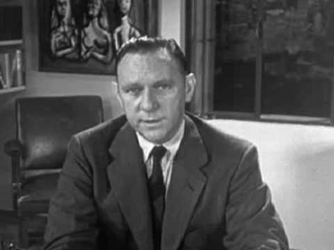 Man in suit talking directly to camera, 1950s business or political scene.