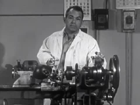 Worker operating heavy machinery lathe in a factory or workshop, 1950s.