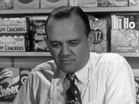A grocery store clerk looking down thoughtfully while working behind the counter.