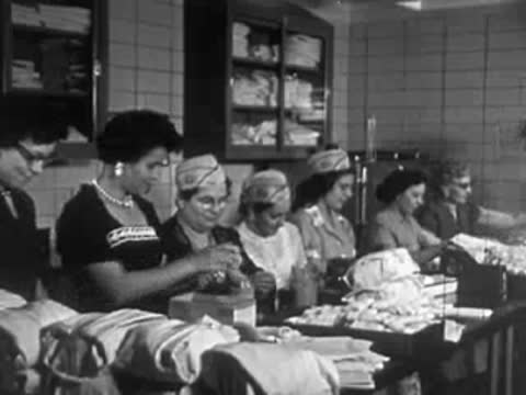 Women in aprons working along a conveyor belt or assembly line in a food facility.