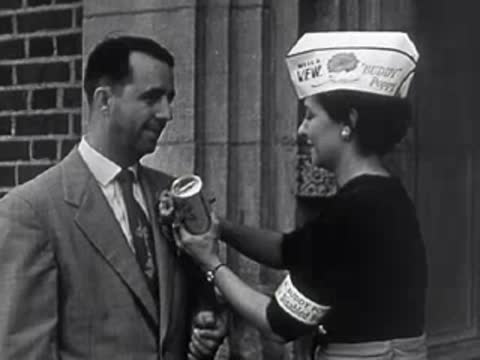 A woman pinning a Buddy Poppy flower onto a man's suit jacket outdoors.