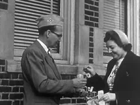 A woman in a uniform pinning a charity flower onto a veteran's lapel outside.