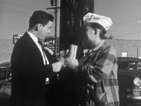 A woman in a plaid jacket distributing Buddy Poppy pins to a man outdoors.