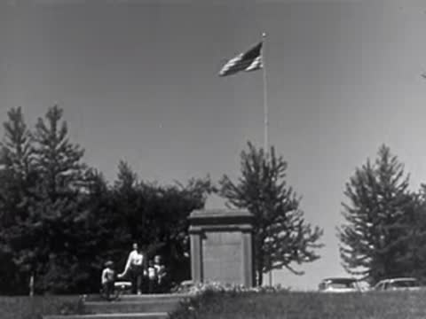 An American flag waving on a tall flagpole outside a stone monument memorial.
