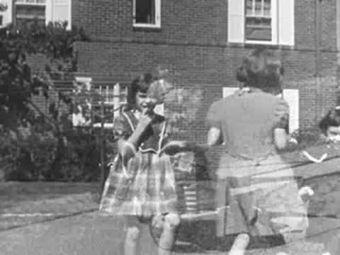 Children playing outdoors near a brick home, with a child riding a toy car.