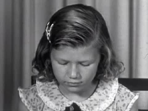 A young girl sitting at a table with a decorative floral collar, looking down.