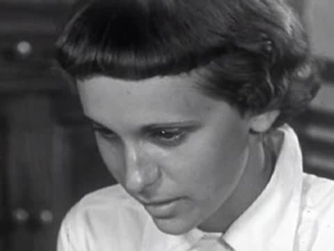 Close-up of a young girl looking downward with a pensive expression indoors.
