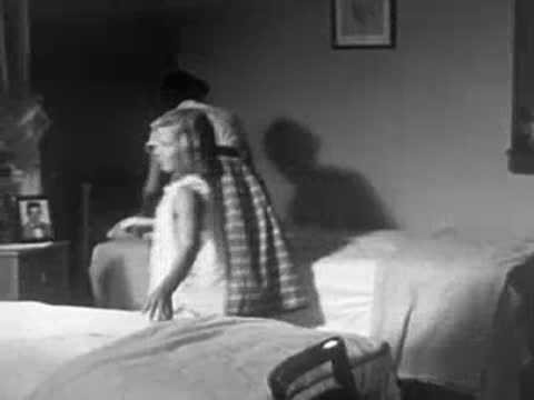 A woman helping a young girl get ready in a bedroom with twin beds.