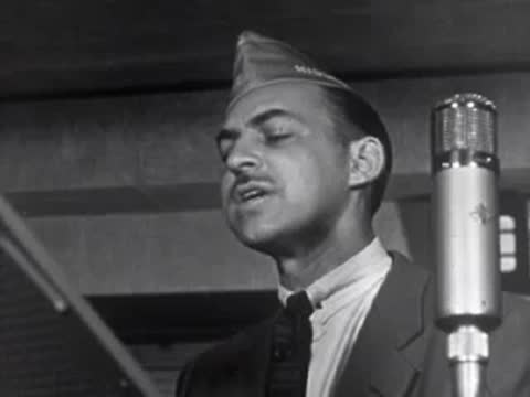 A man in a military-style cap speaking into a vintage microphone.