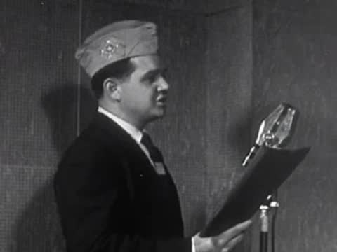A man in a suit and service cap reading from a document into a microphone.