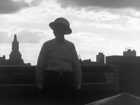 Silhouette of a person in a hat standing on a rooftop against a skyline.
