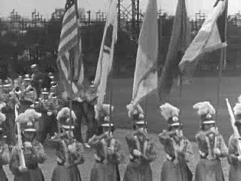 A marching band with flags and instruments lined up on a large field.