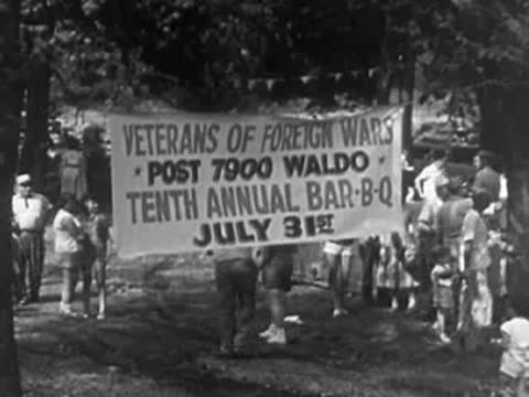People walking in a parade next to a banner for veterans of foreign wars.