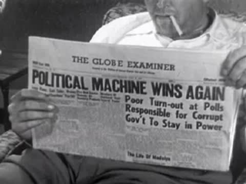 Close-up of newspaper being read with headline "Political Machine Wins Again", 1950s.