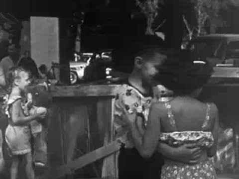 Children interacting outdoors near a wooden fence at a community gathering.
