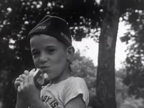 Young boy in cap and t-shirt eating ice cream outdoors, 1950s.