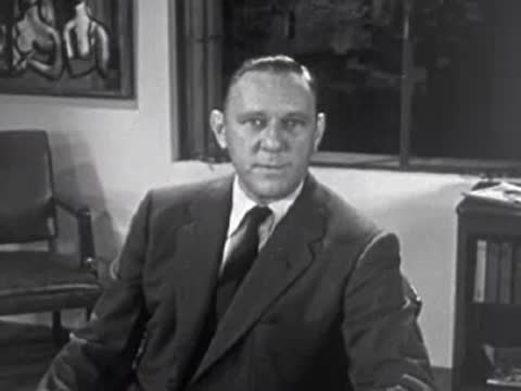 Man in suit jacket and tie sitting in an office, 1950s.