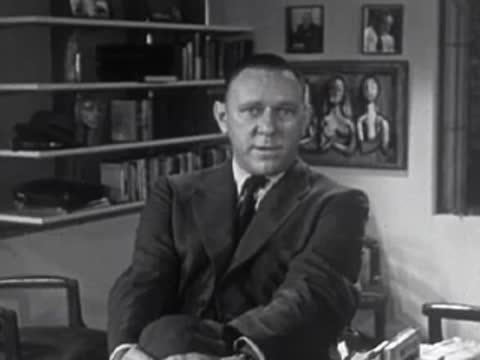 Man in suit sitting in an office speaking, 1950s.