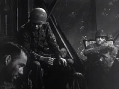 Soldiers in helmets seated indoors looking down, 1950s.