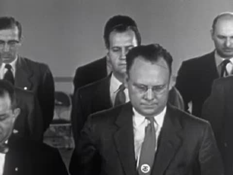 Men in suits standing and lowering their hands, 1950s.