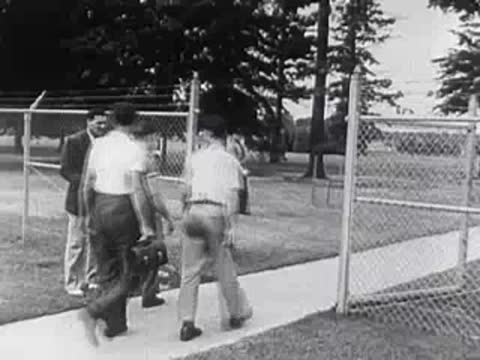 Two men carrying toolboxes walking along a fence on a campus