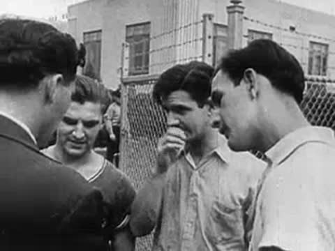 Close-up conversation between young men near a wire fence outdoors