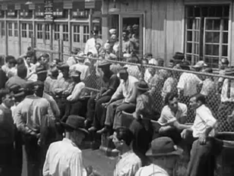 Large crowd of men sitting and standing near a chain link fence