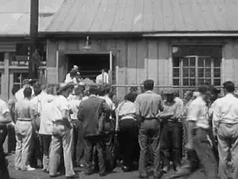 Workers gathered outside an industrial building, conversing in groups