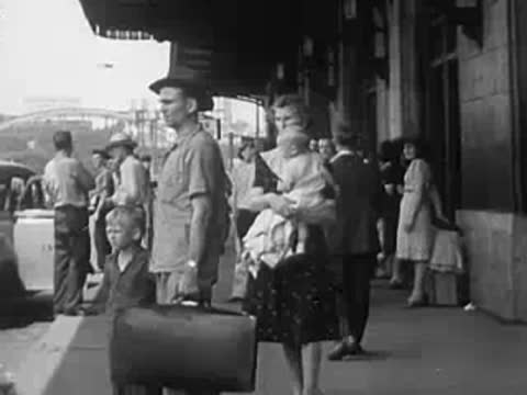 Family with luggage walking on a street, WWII era street scene