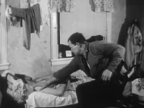 Man standing in a modest room, another person resting in bed