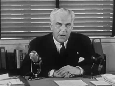 Man in suit speaking behind a desk with a microphone