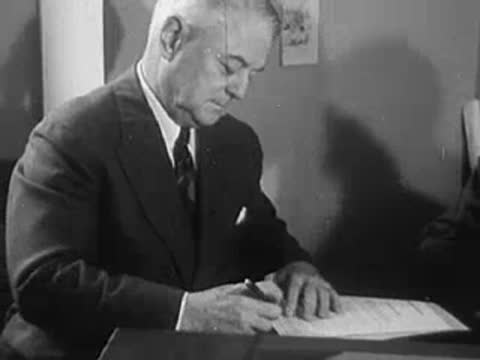 A man sitting at a desk writing or signing documents, office.
