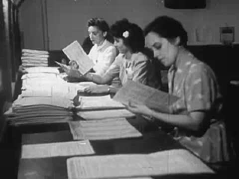Three women seated at a table examining documents or files in office.