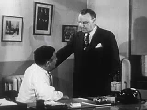 A man standing next to a seated man in an office.